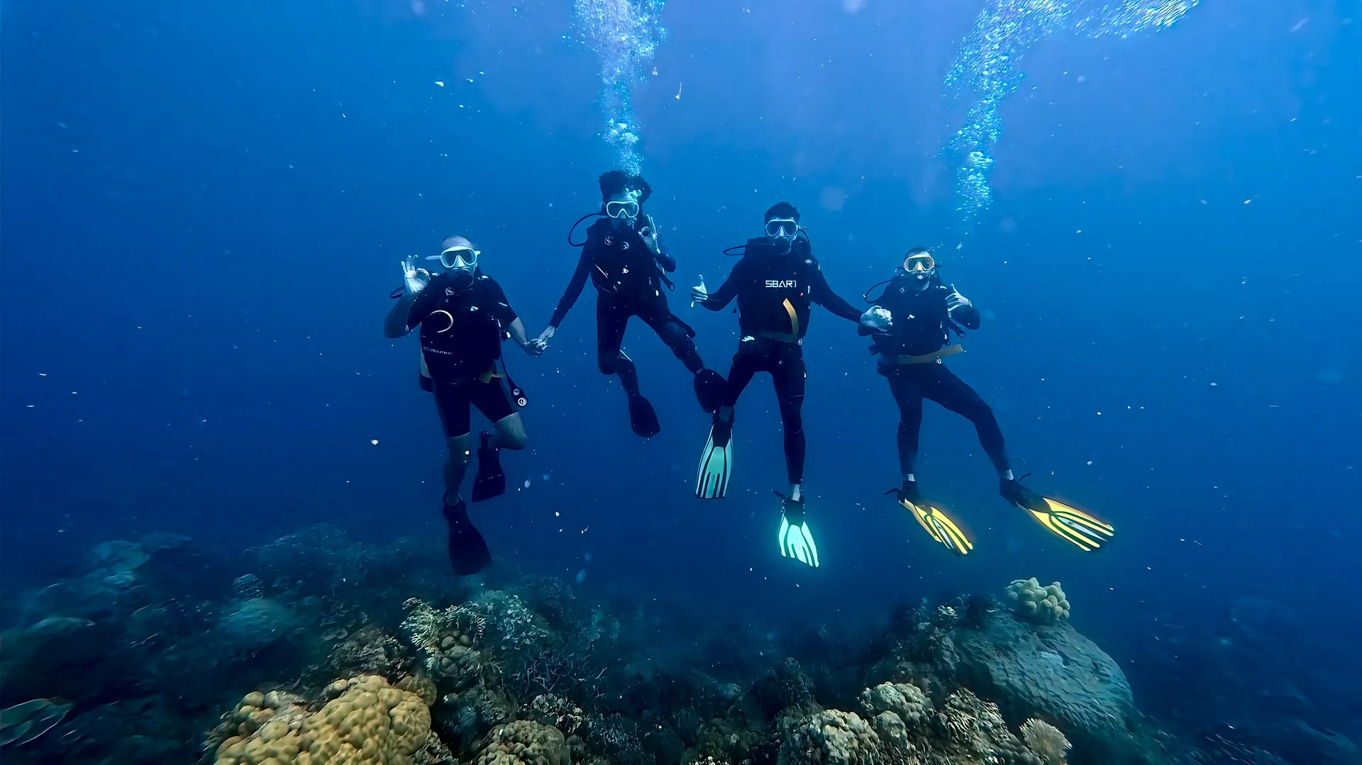 Four divers swimming together over a reef