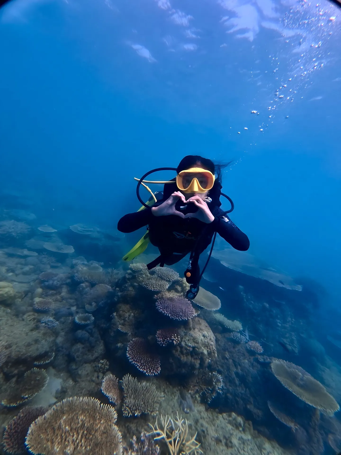 Diver making a heart with her hands over a coral reef