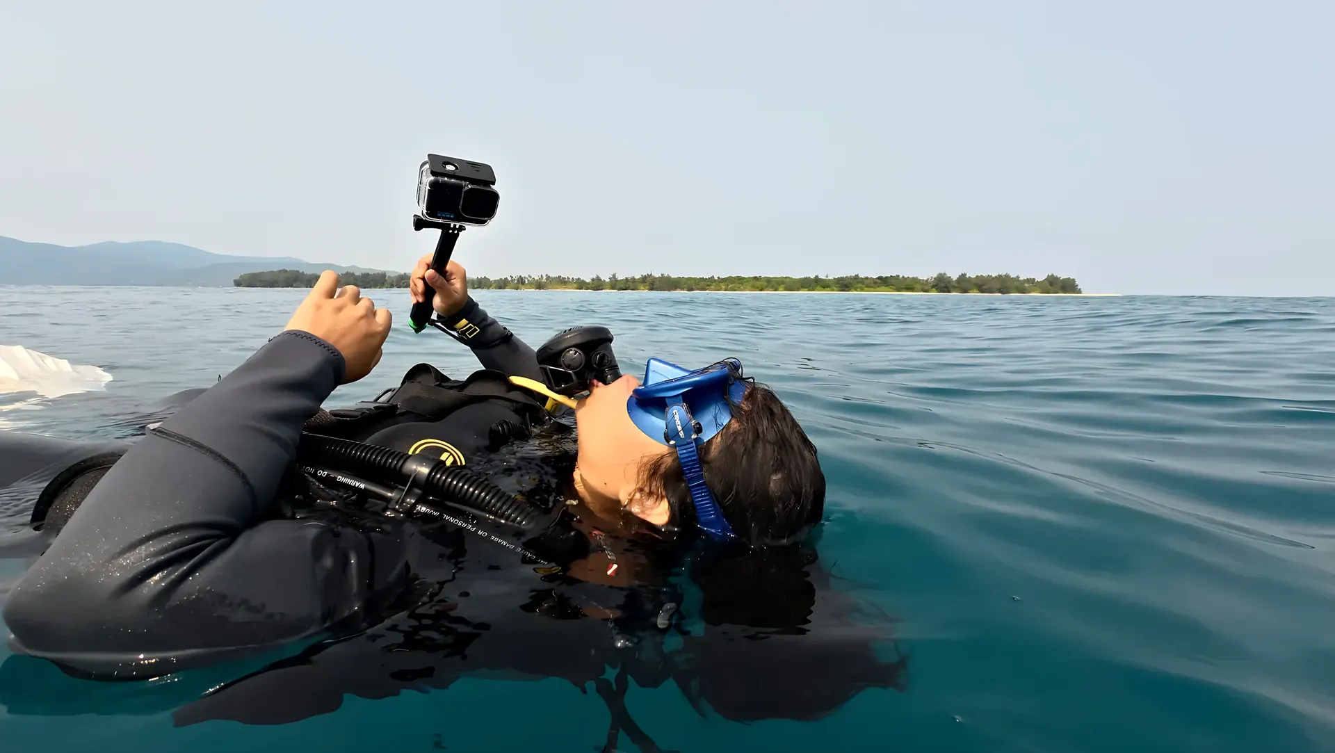 Diver floating at the surface with a camera and a Karimunjawa island in the background